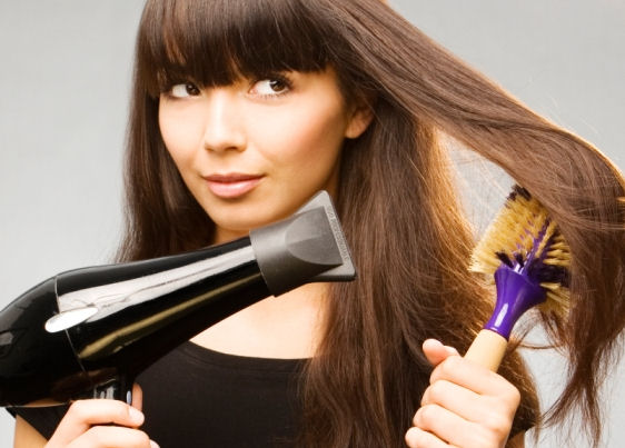 Mulher de cabelo comprido e castanho escuro segura escova com a mão esquerda e secador com a mão direita